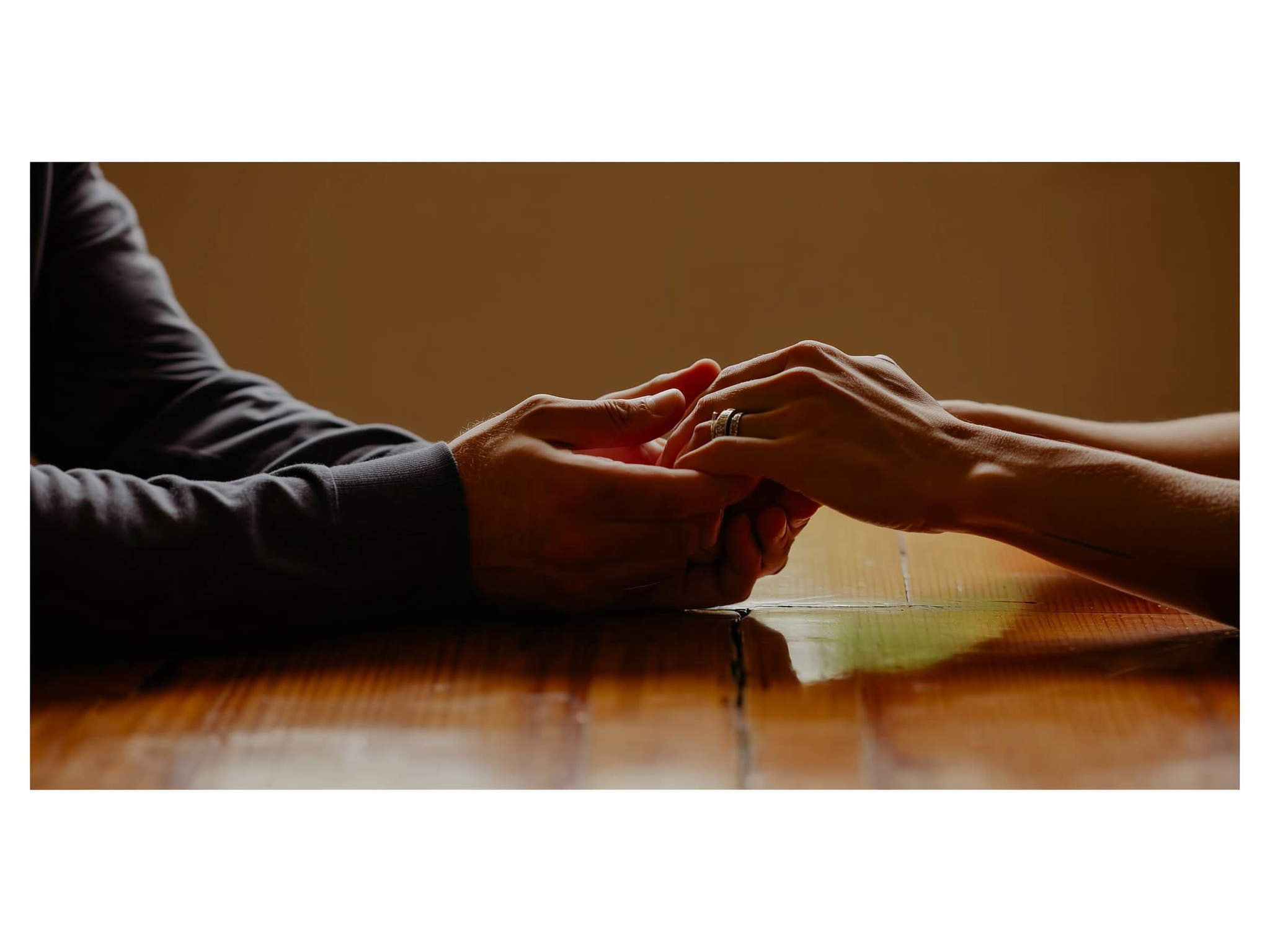 Manos entrelazadas sobre una mesa, mostrando conexión y esperanza en la pareja