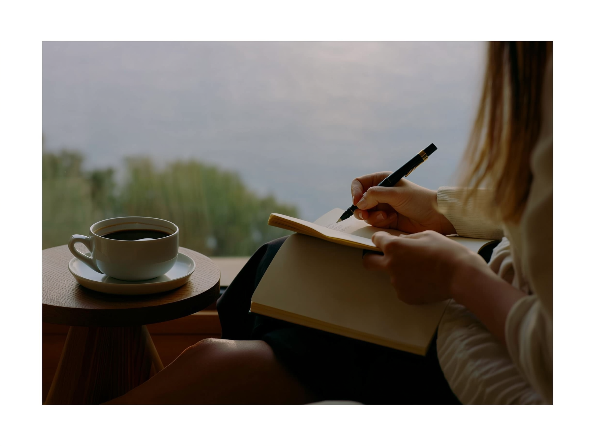 Manos escribiendo en diario personal con café matutino