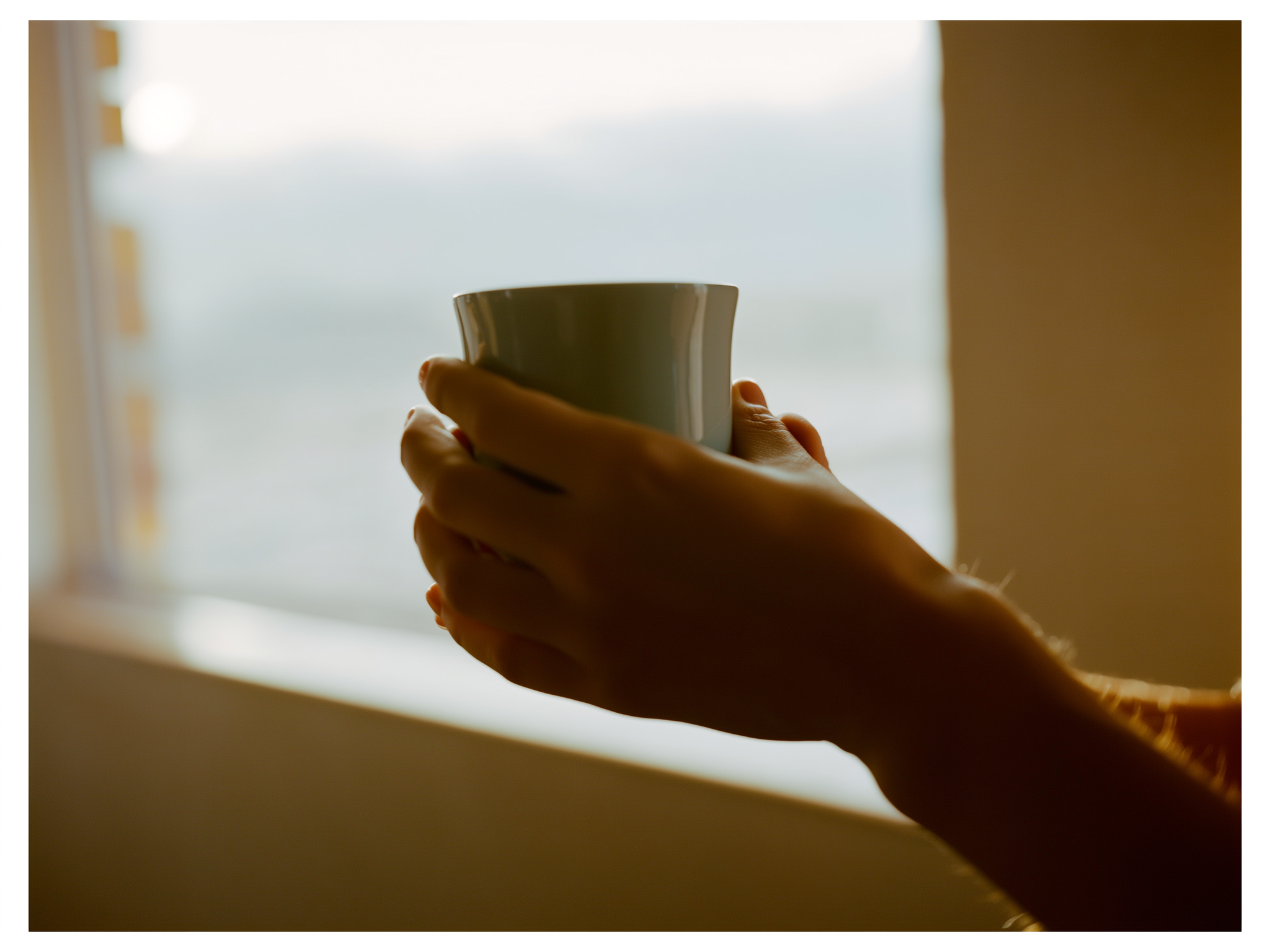 Manos sosteniendo taza de té junto a ventana con luz suave