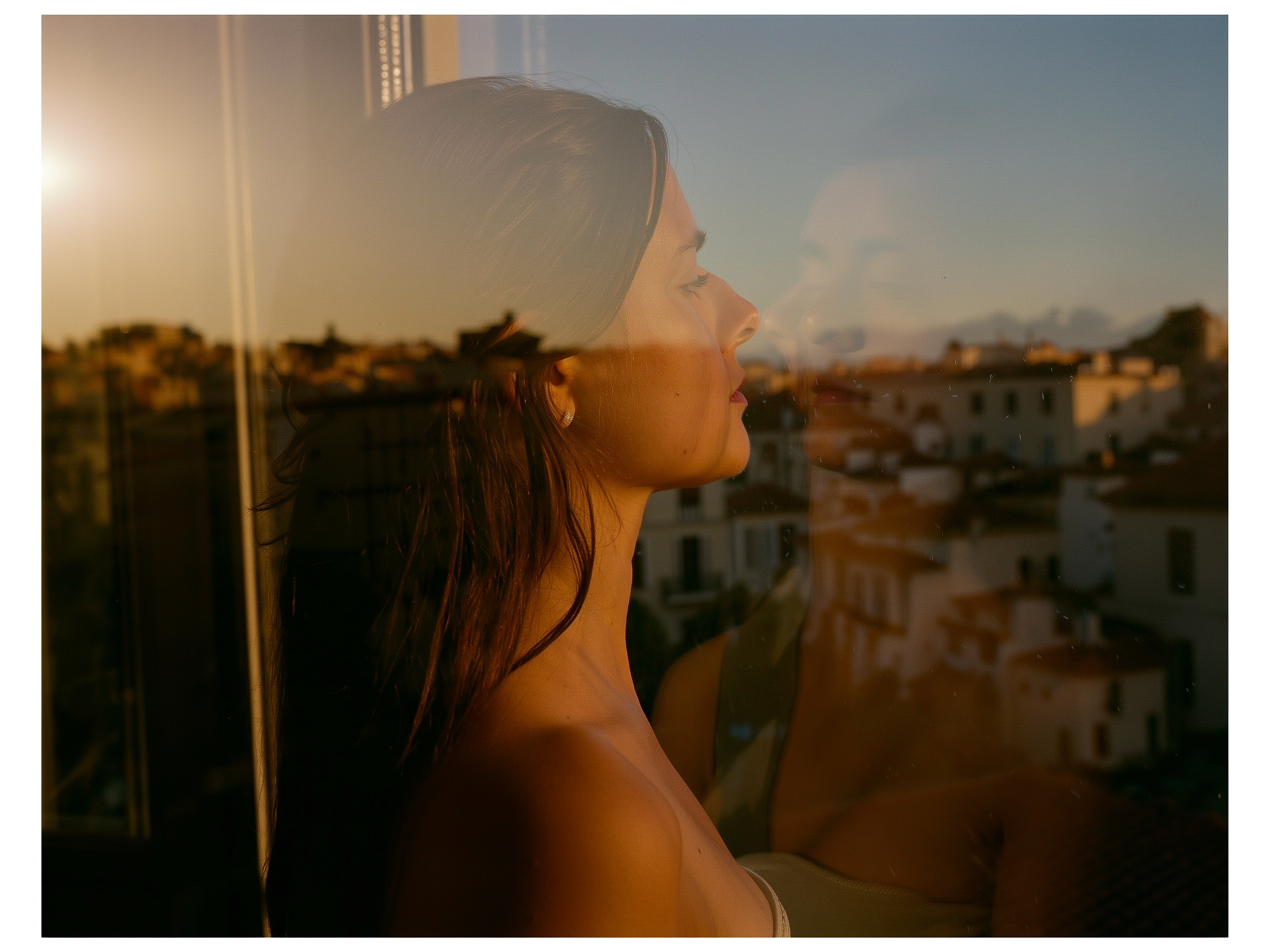 Reflexión de una mujer en la ventana durante el atardecer, simbolizando la introspección