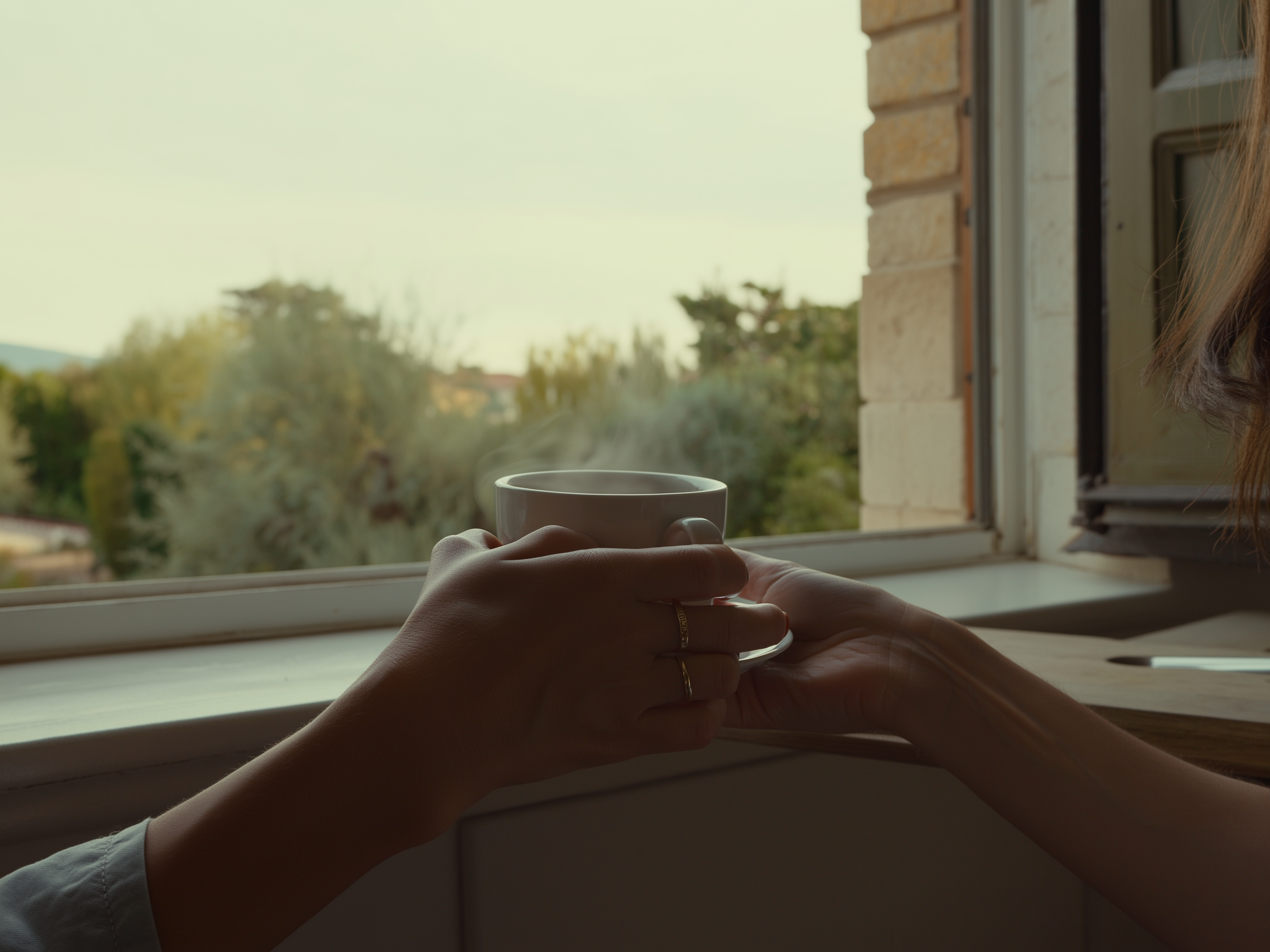 Manos femeninas sosteniendo una taza de té junto a la ventana con luz natural