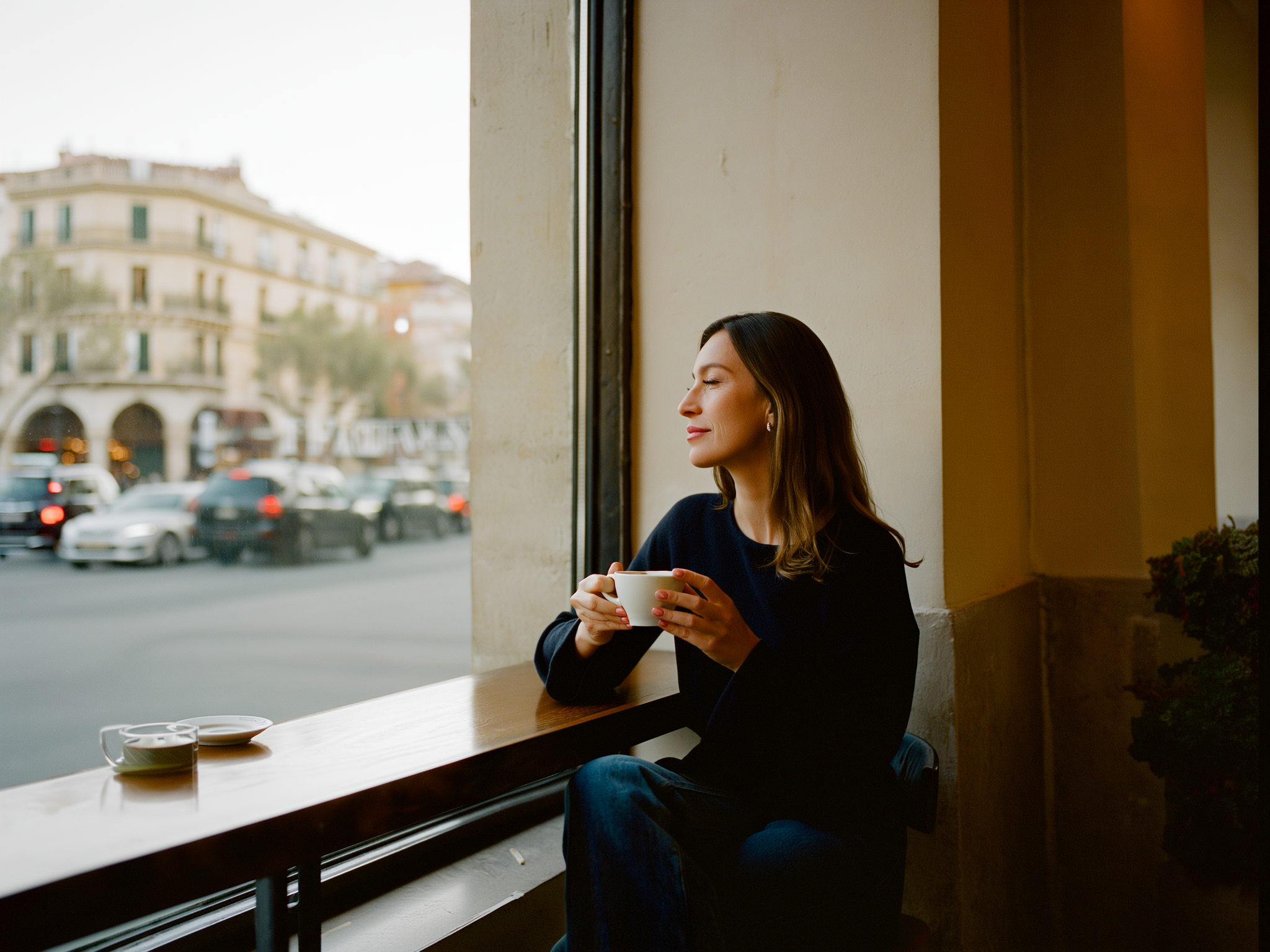 Mujer joven disfrutando de un momento de tranquilidad en una cafetería con una taza de té, luz suave de ventana