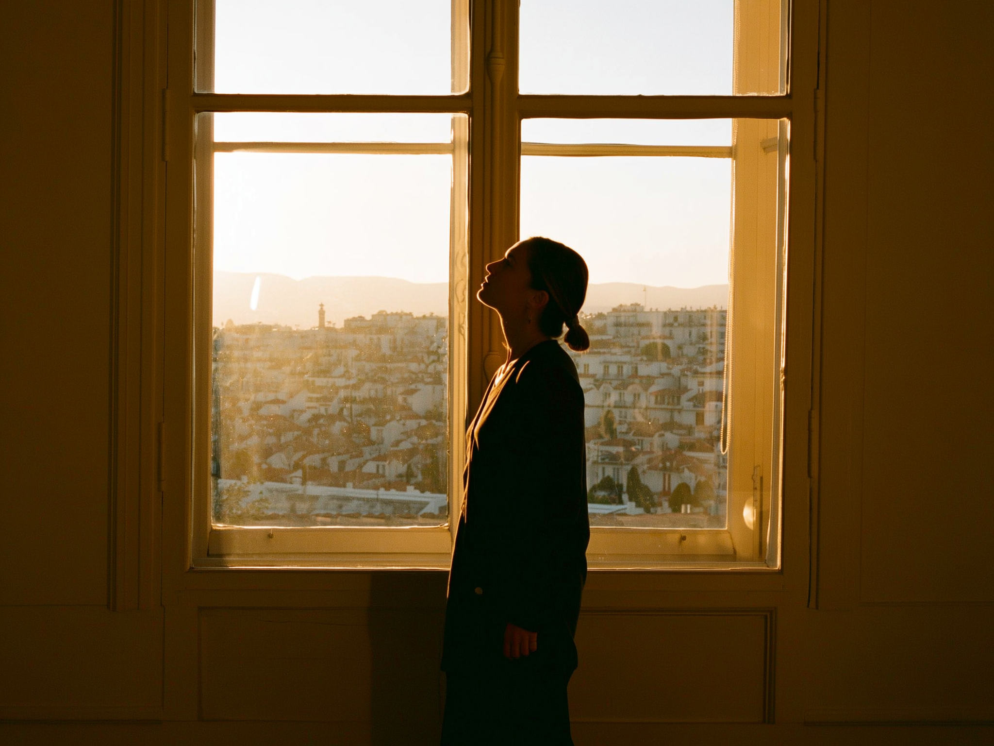Mujer tranquila mirando por la ventana con luz suave, representando esperanza y calma en el proceso de maternidad