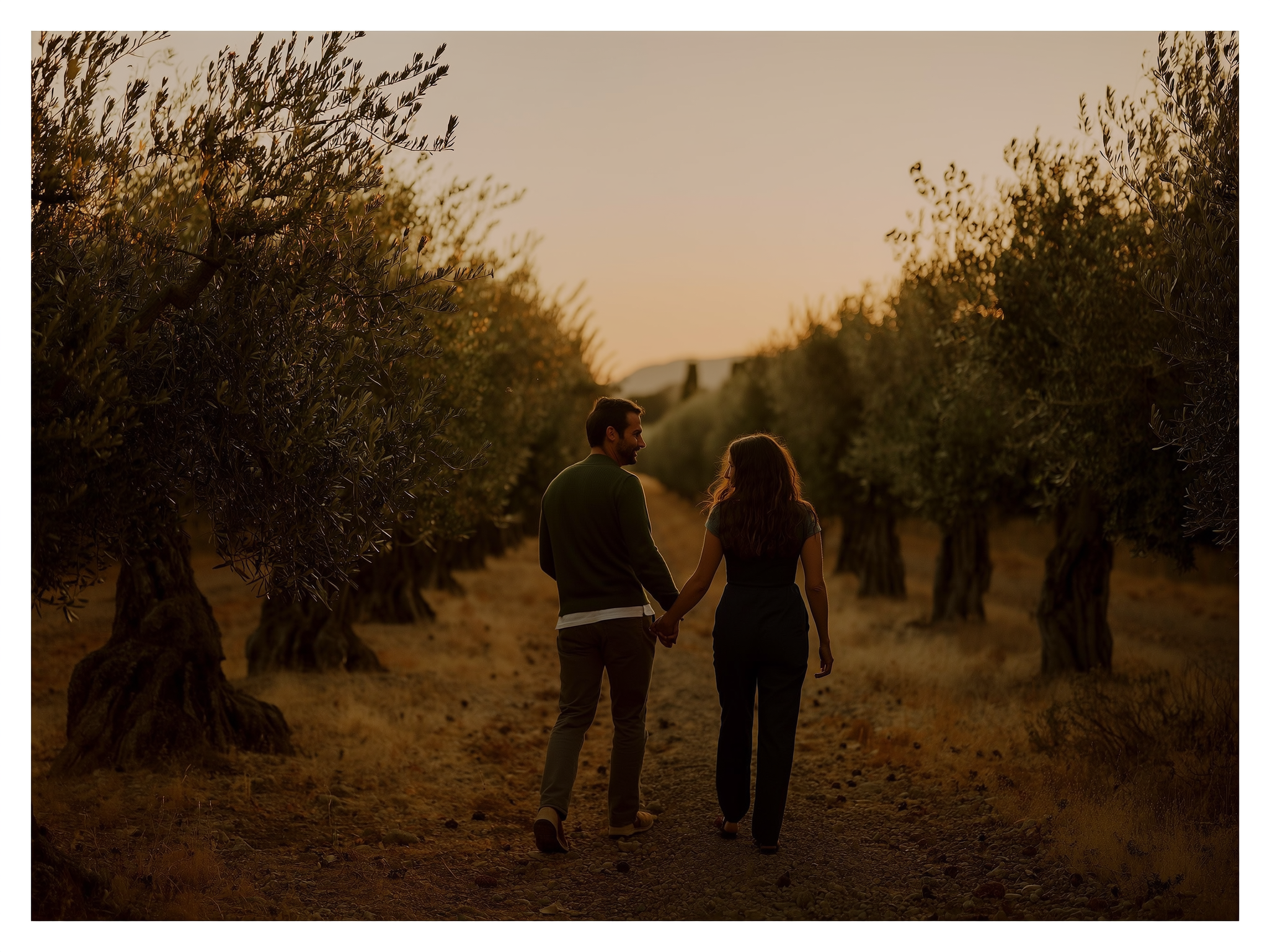 Pareja de la mano caminando entre olivos al atardecer, simbolizando unión y tranquilidad