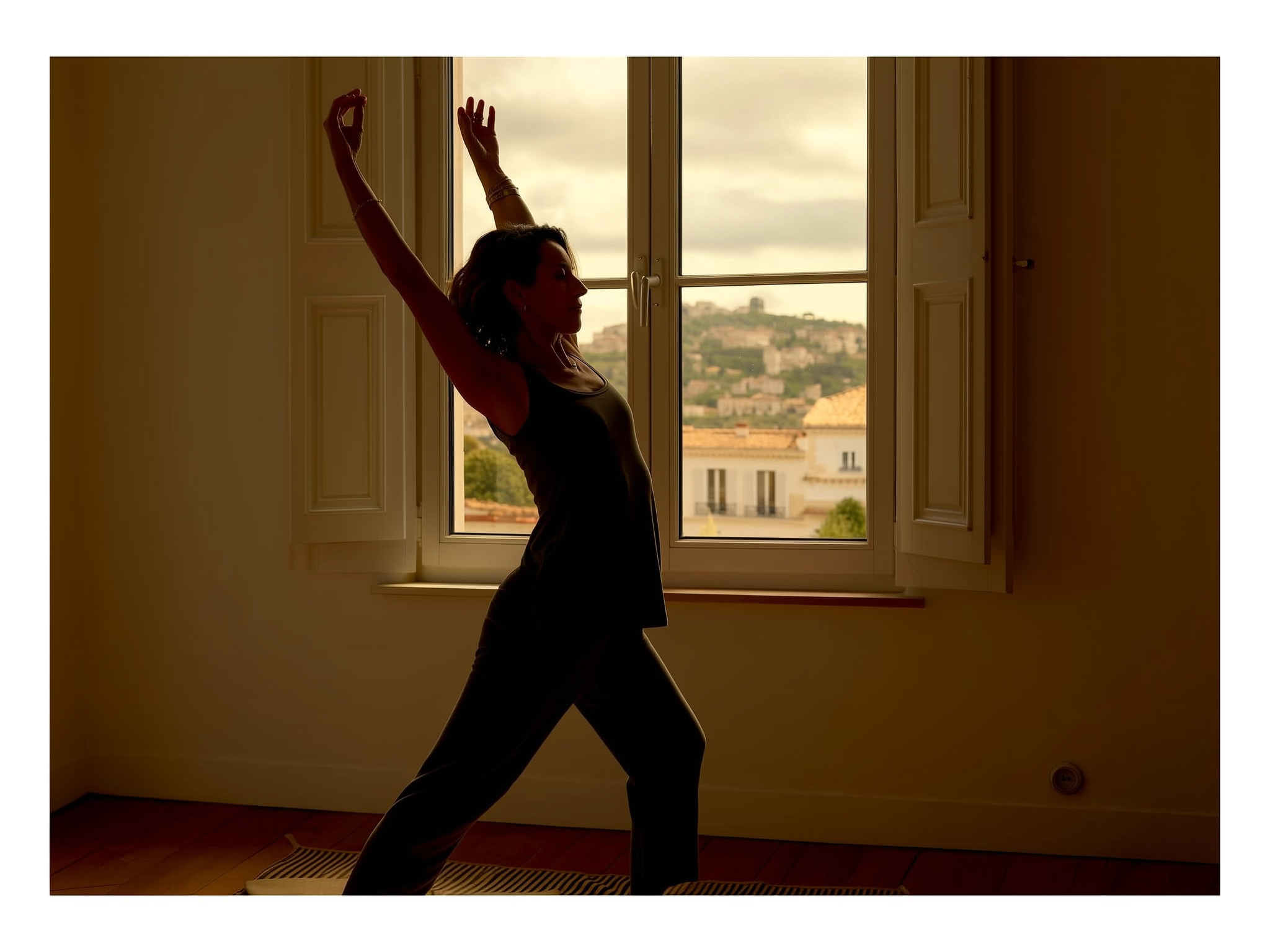 Silueta de mujer haciendo estiramientos suaves junto a una ventana con luz natural