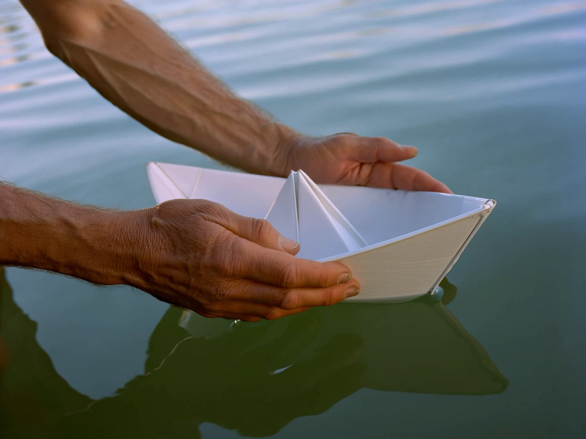 Manos protegiendo un barco de papel en aguas tranquilas, representando el cuidado delicado en las relaciones