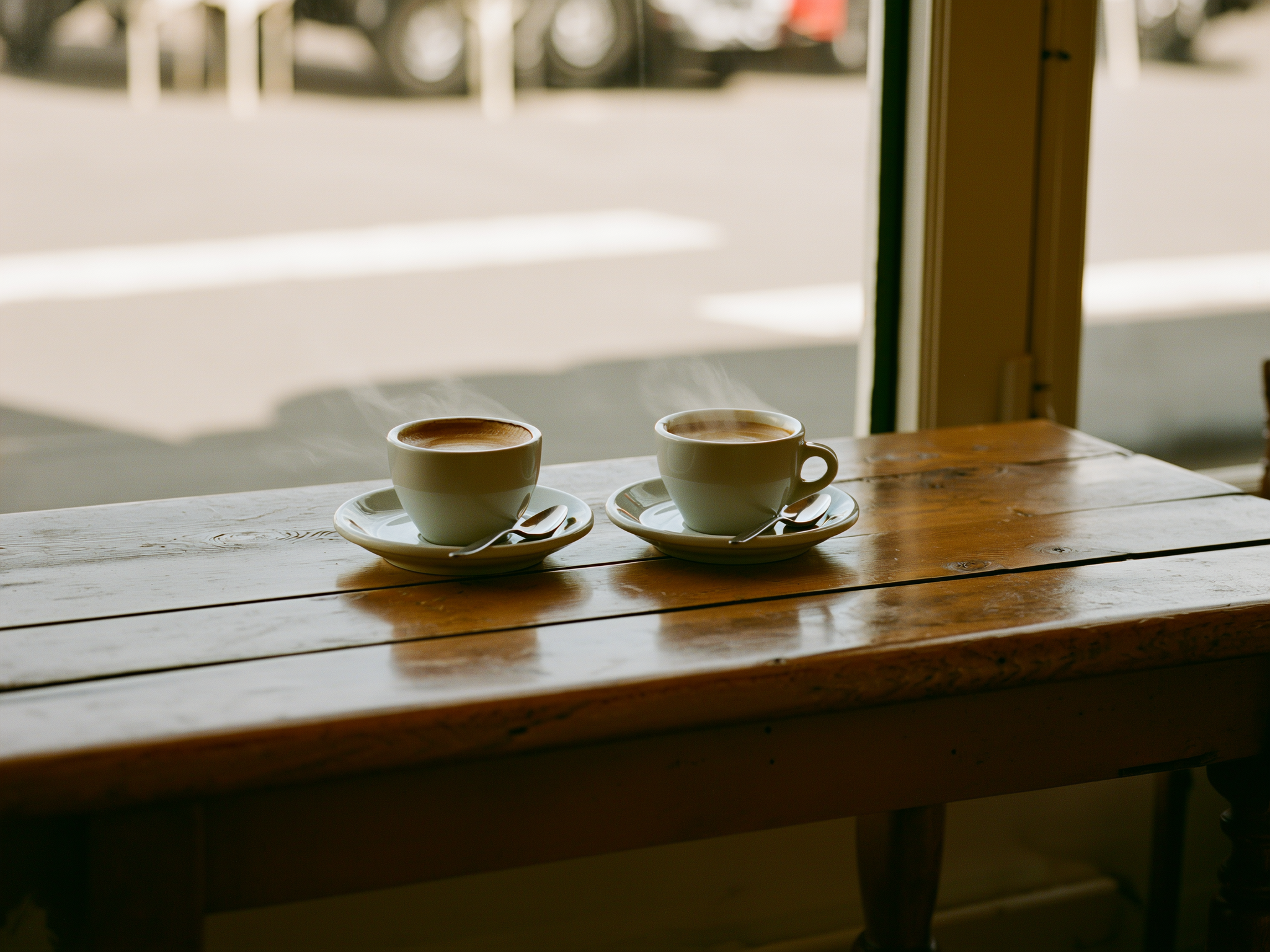 Dos tazas de café en una mesa junto a la ventana, una humeante y otra intacta, simbolizando la conexión y la paciencia