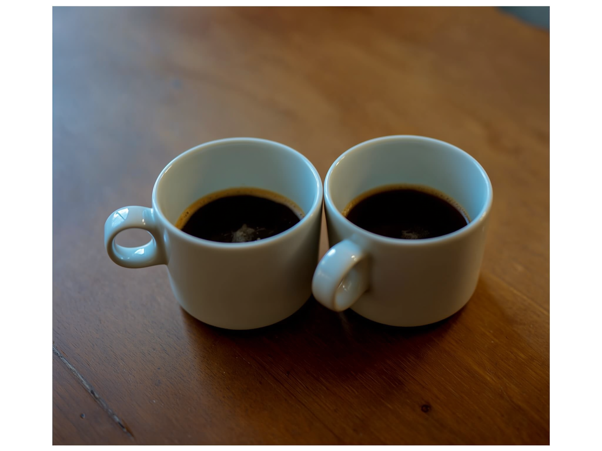 Dos tazas de café separadas en una mesa de madera simbolizando la distancia en la comunicación de pareja
