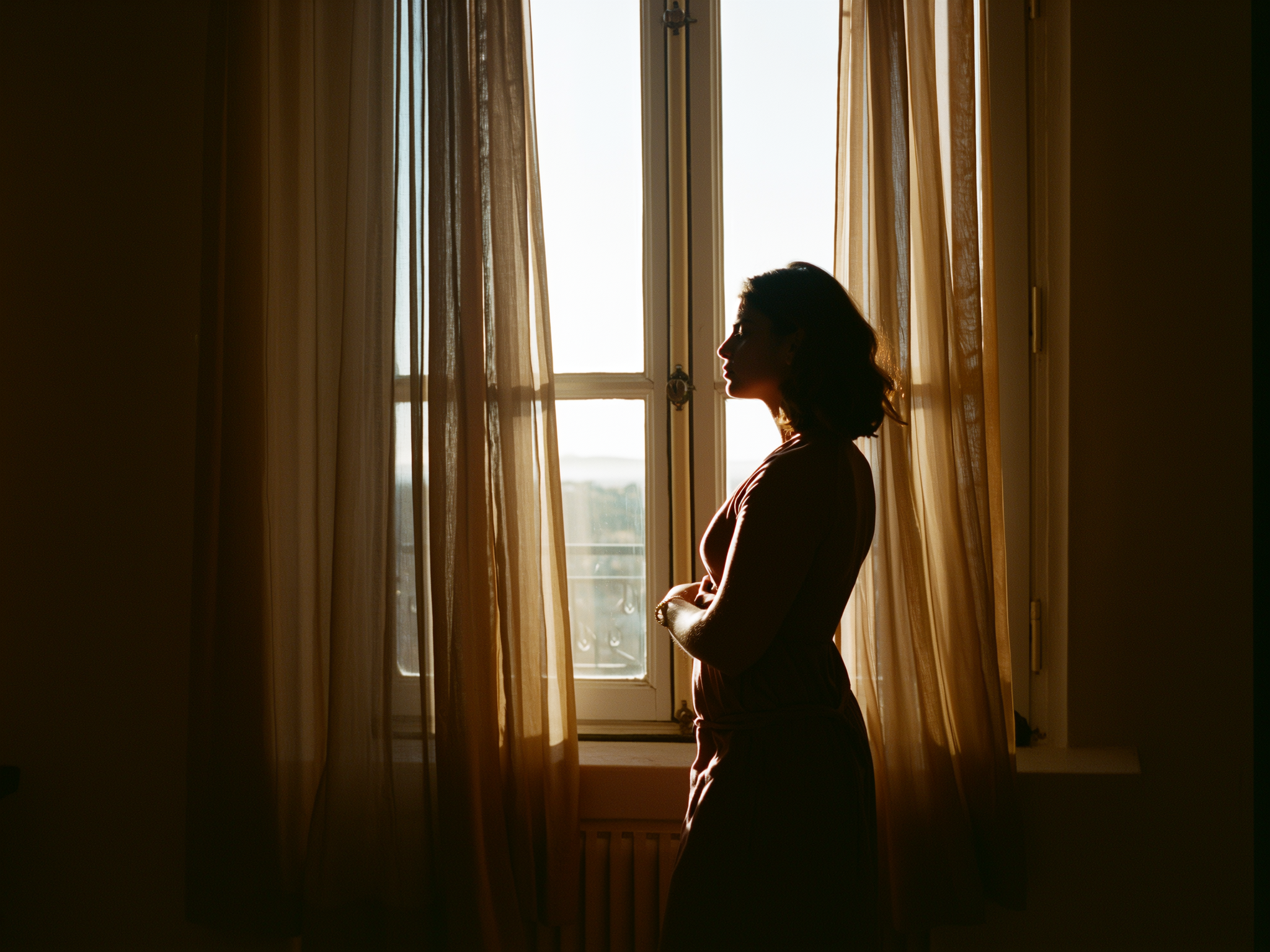 Mujer contemplativa mirando por ventana con luz suave, simbolizando reflexión y esperanza