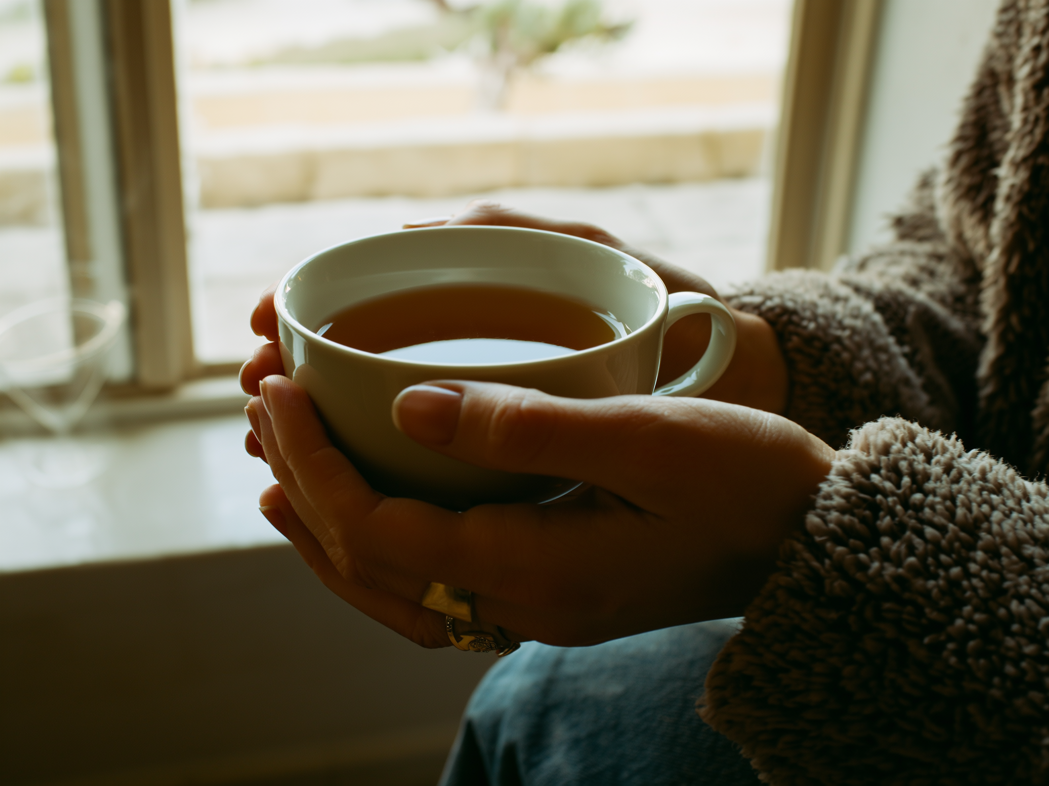 Manos sosteniendo una taza de té junto a una ventana con luz natural