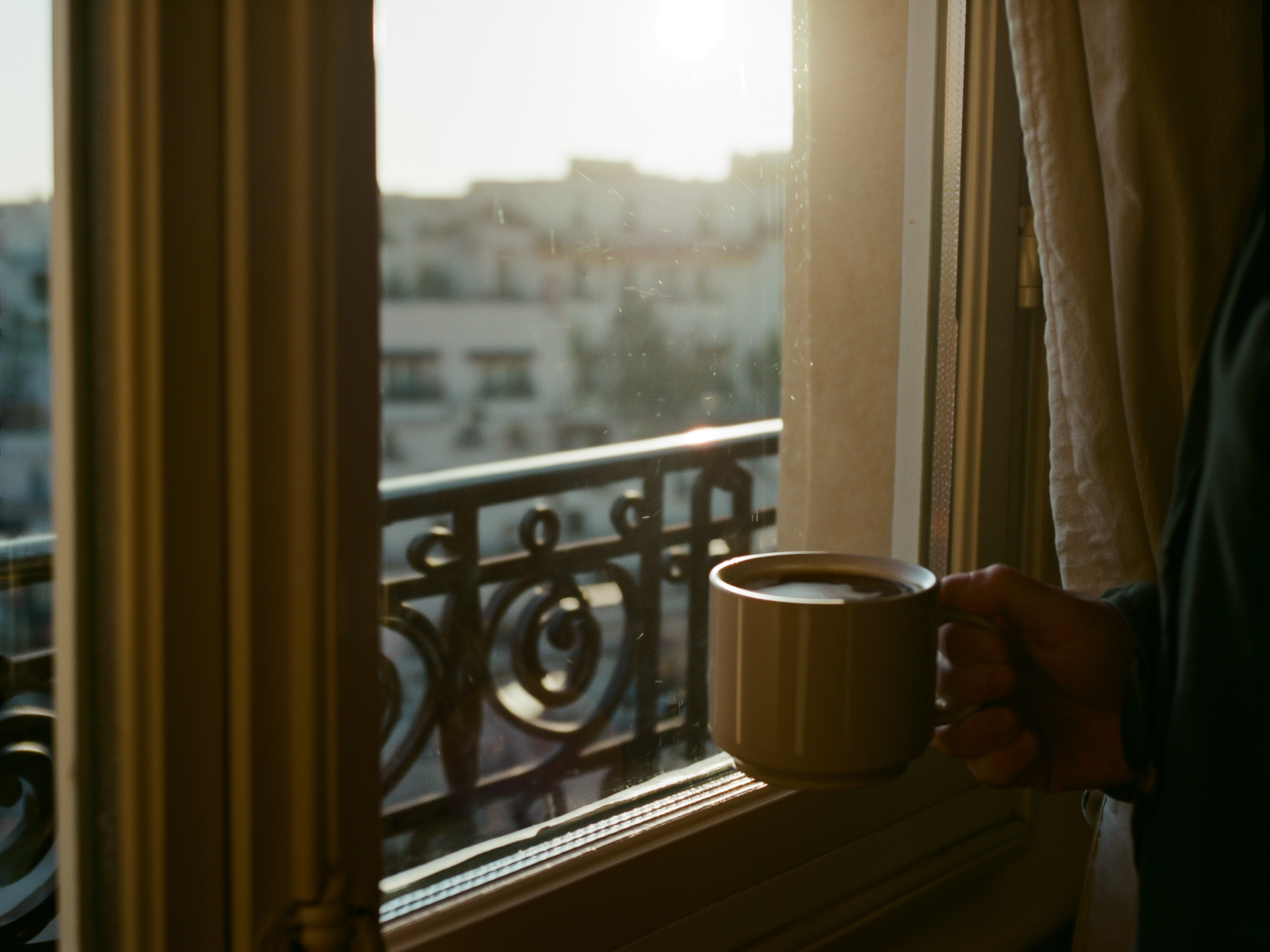 Manos sostienen taza de café junto a ventana en momento de reflexión matutina