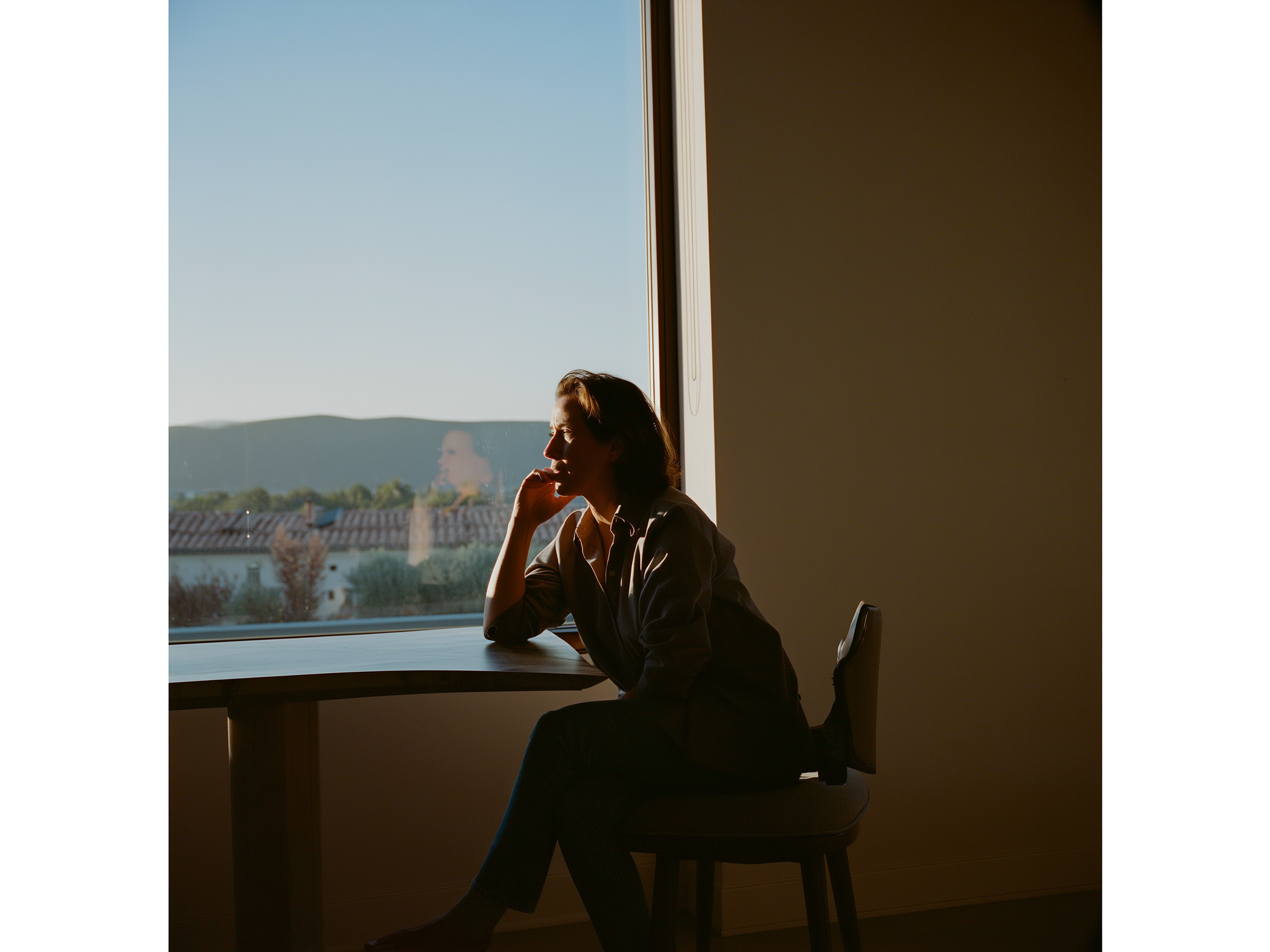 Mujer joven reflexionando en soledad junto a una ventana con luz natural