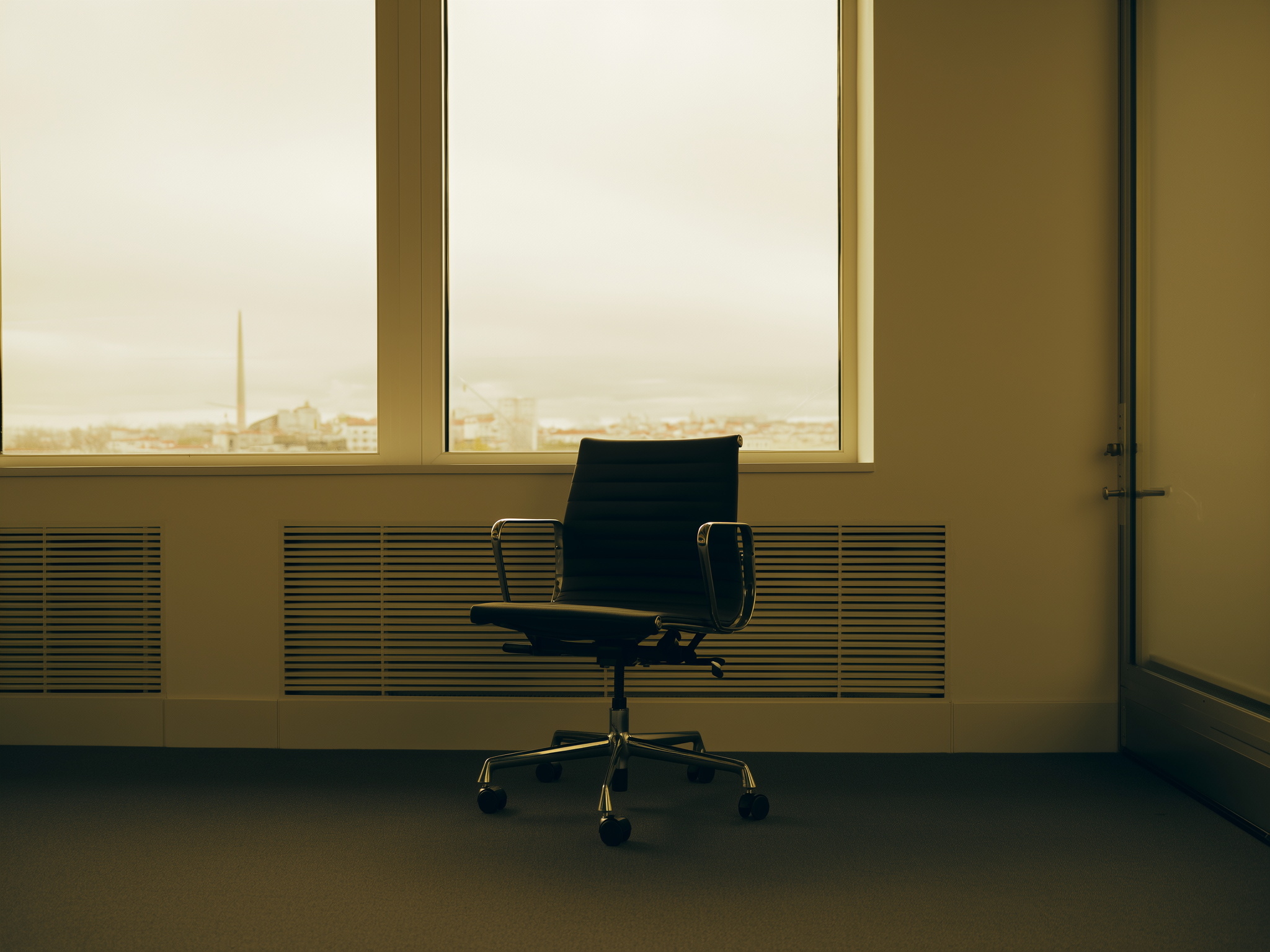 Persona contemplando por una ventana de oficina con expresión melancólica pero vestida profesionalmente
