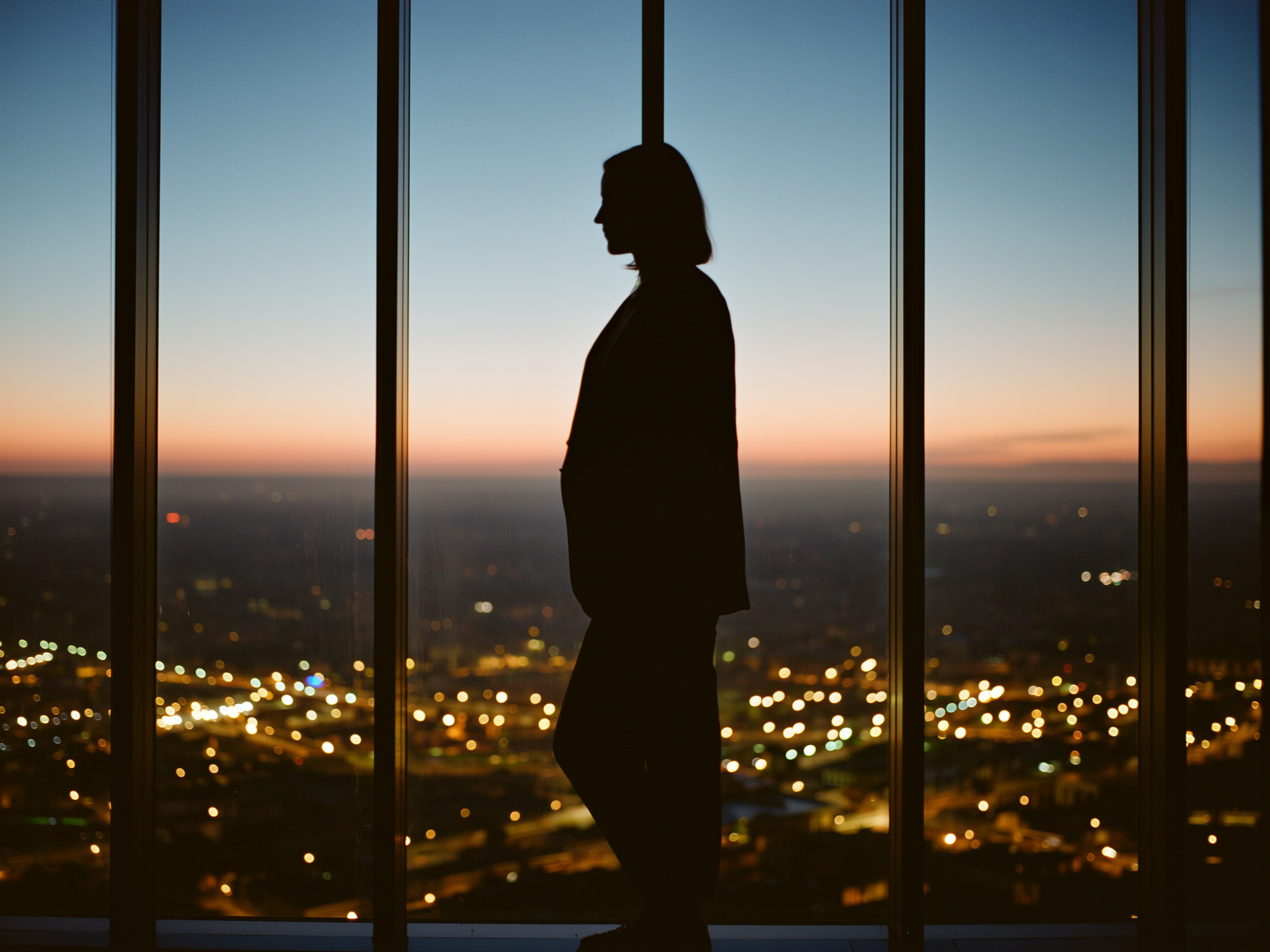 Silueta de mujer profesional contemplando la ciudad desde oficina al atardecer