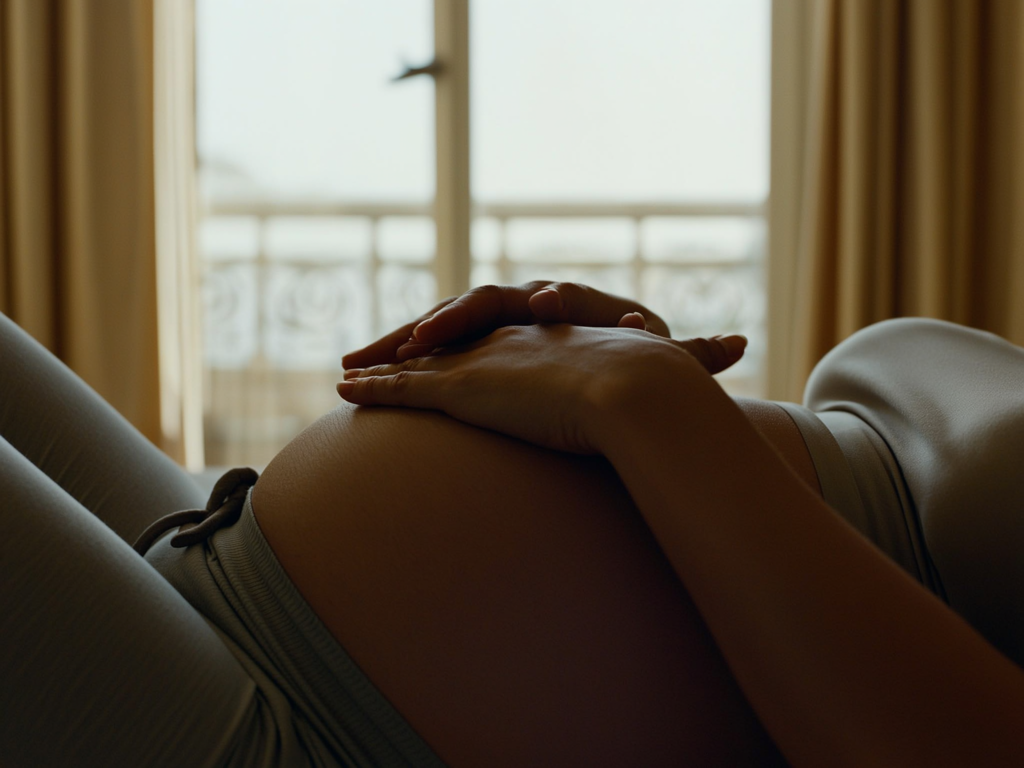 Manos de mujer embarazada descansando sobre su vientre con luz natural suave