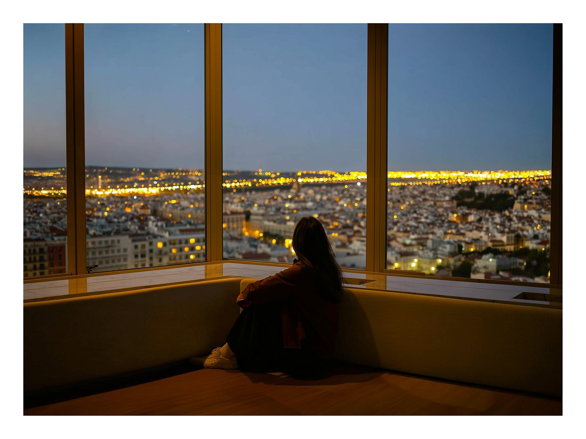 Mujer sola en apartamento moderno mirando las luces de la ciudad al atardecer