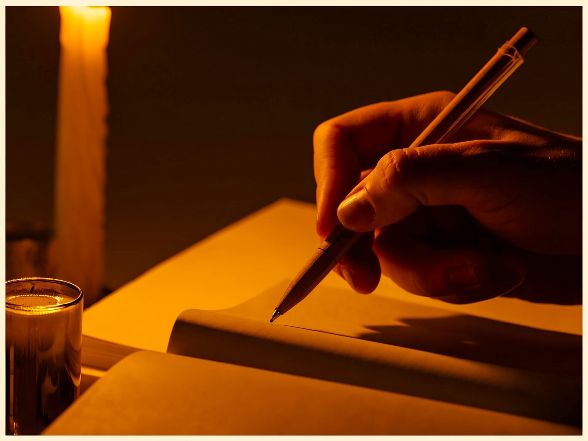 Manos escribiendo en un diario a la luz de velas, simbolizando la reflexión y el proceso interno