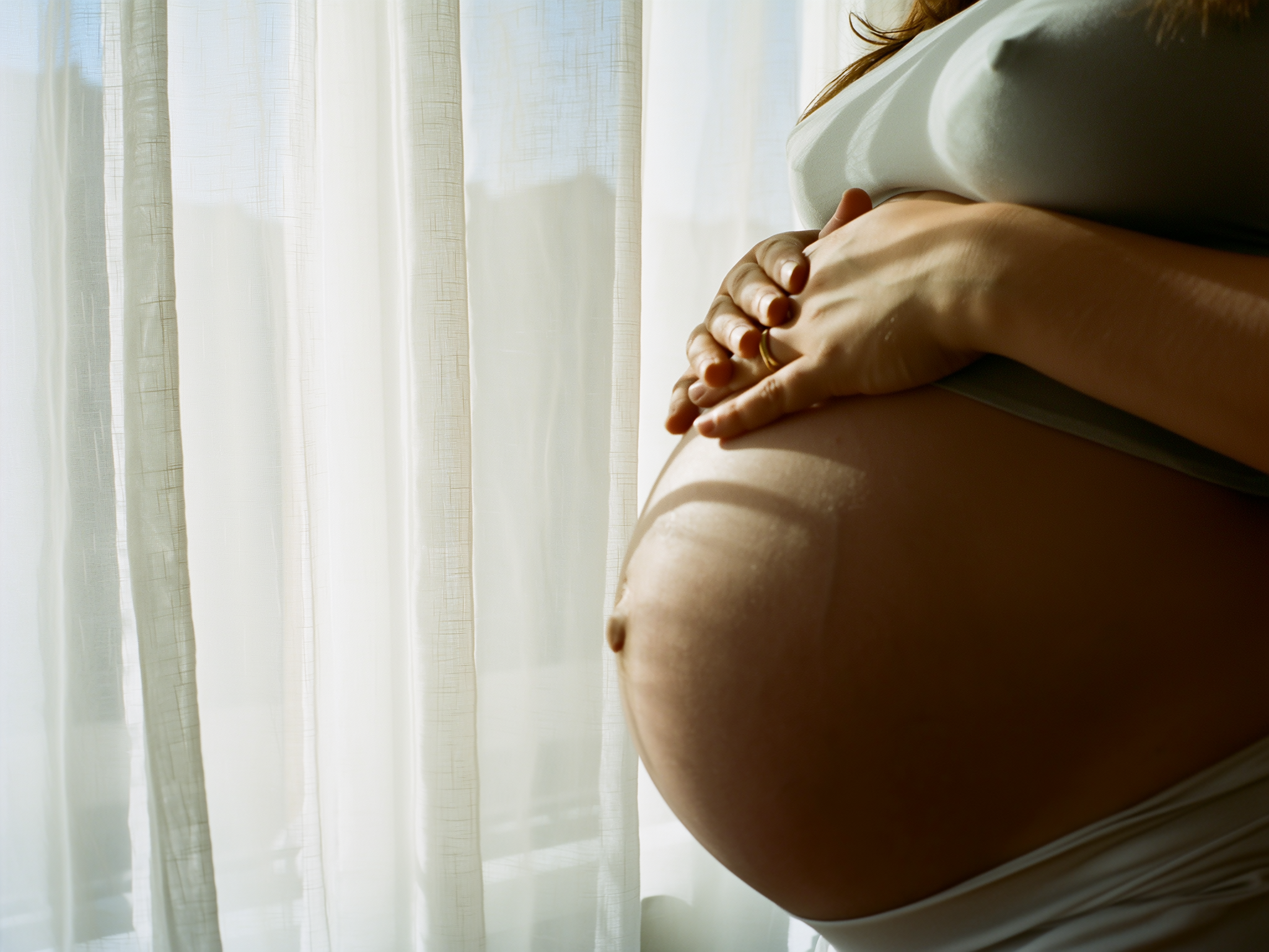 Manos de mujer embarazada reposando protectoramente sobre su vientre