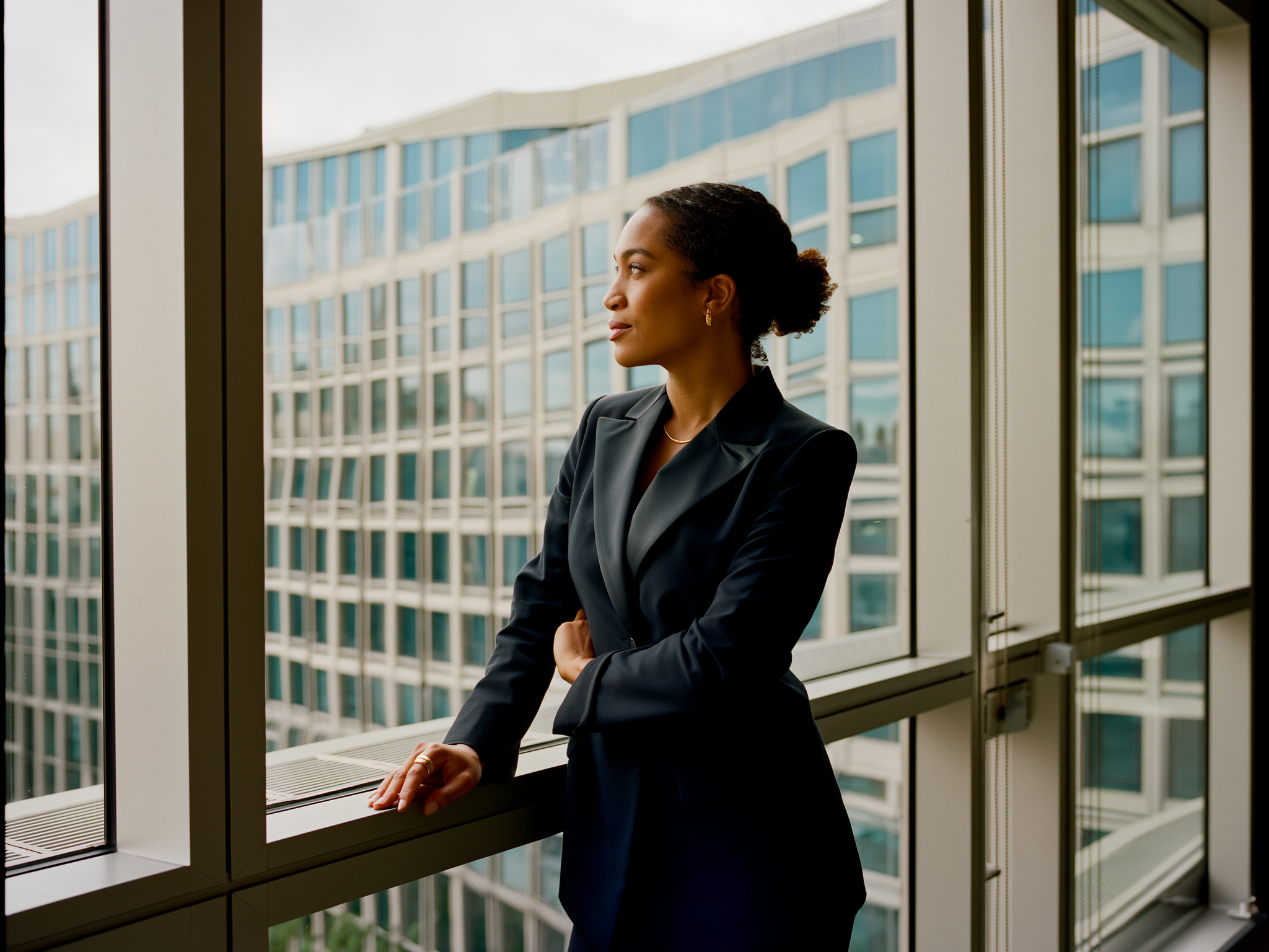 Mujer profesional mirando por ventana de oficina con expresión serena y determinada