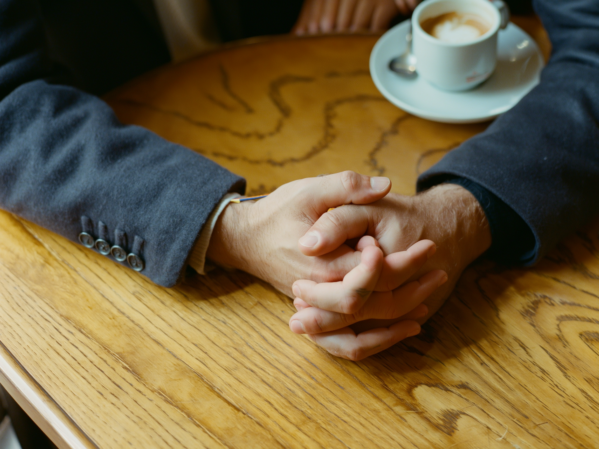 Manos entrelazadas sobre una mesa de madera mostrando tensión emocional en una conversación