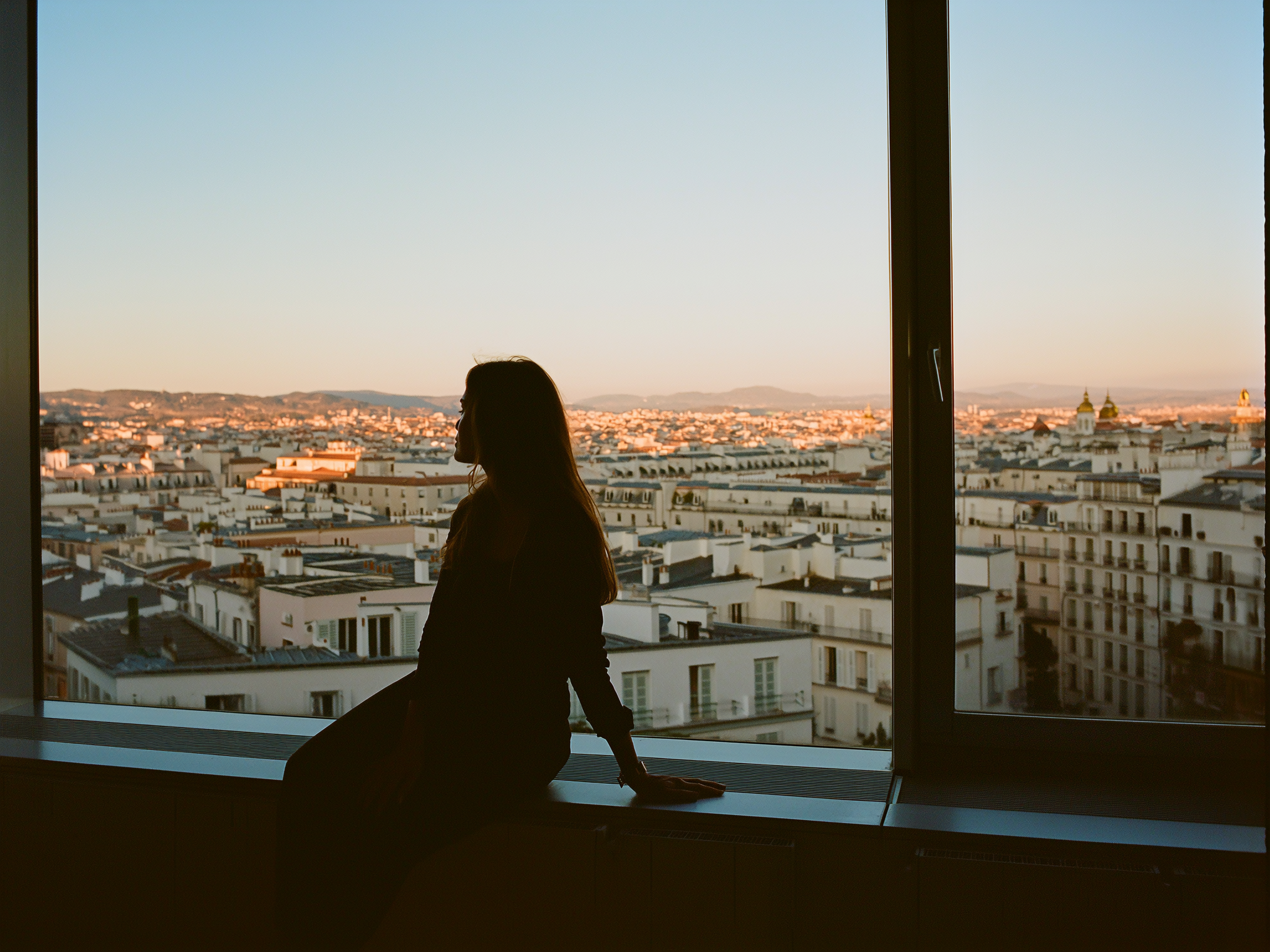 Mujer joven contemplando el horizonte desde una ventana al amanecer, simbolizando reflexión y nuevos comienzos