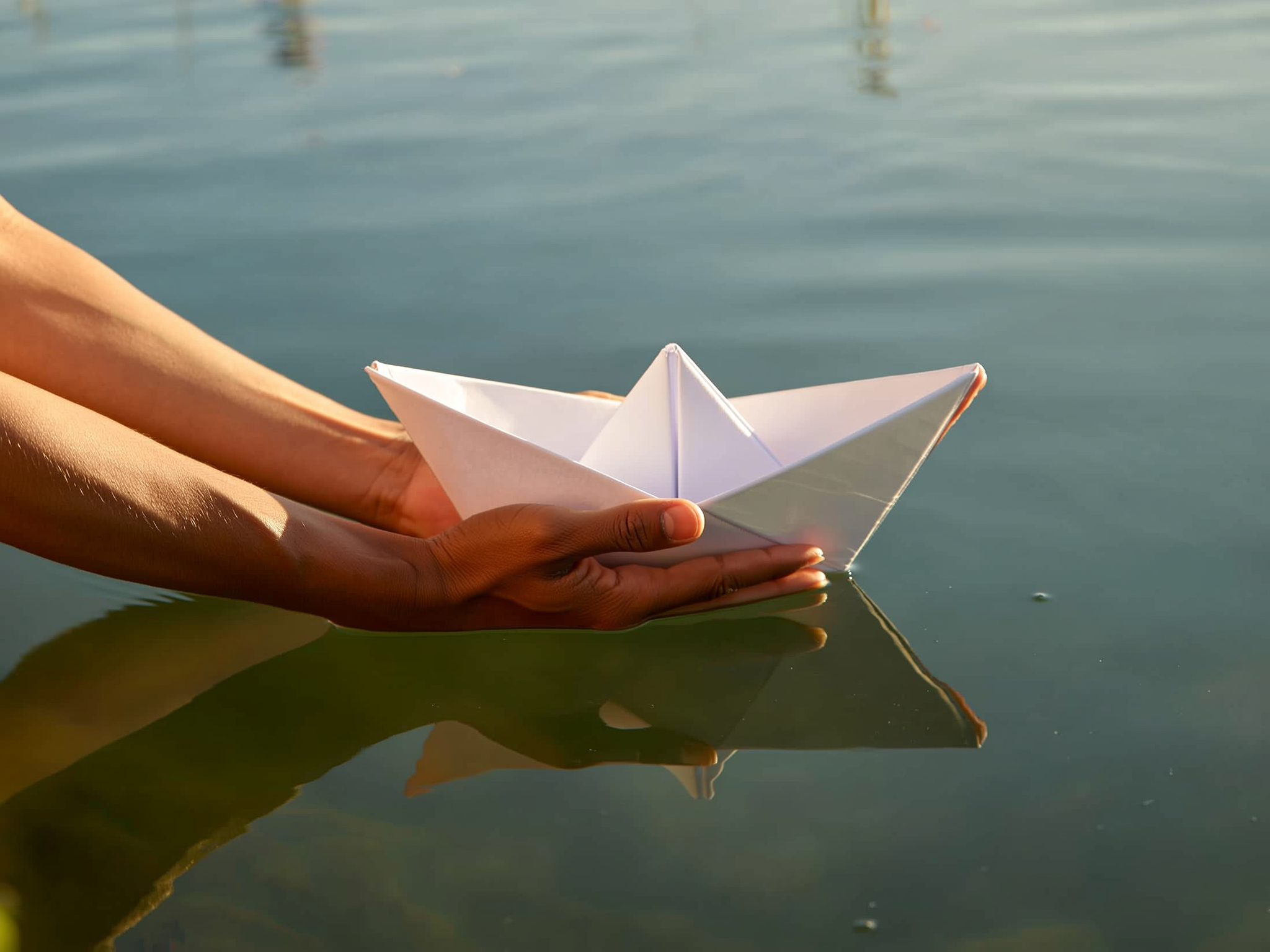 Manos protegiendo un barco de papel sobre agua tranquila, simbolizando cuidado y protección emocional